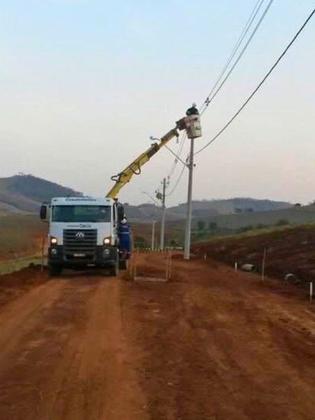 Veículo realizando obra de instalação de postes de energia em área rural